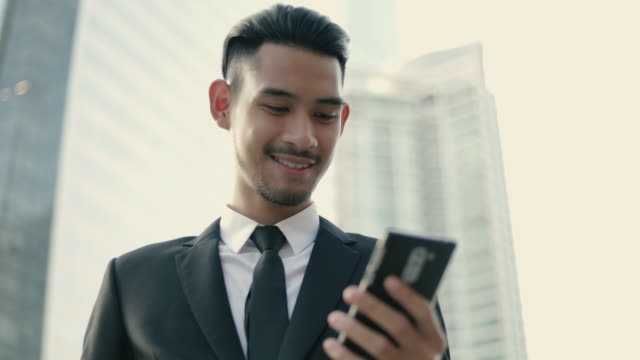 Glücklich-stattlich-junge-Geschäftsmann-mit-einem-Smartphone-SMS-überprüfen-E-Mail-Nachrichten-online-und-nutzt-soziale-Netzwerke,-während-auf-der-Straße-urban-stehen.