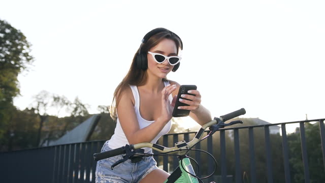 Close-up-of-smiling-young-woman-in-headphones-sitting-on-the-bike-and-listening-music