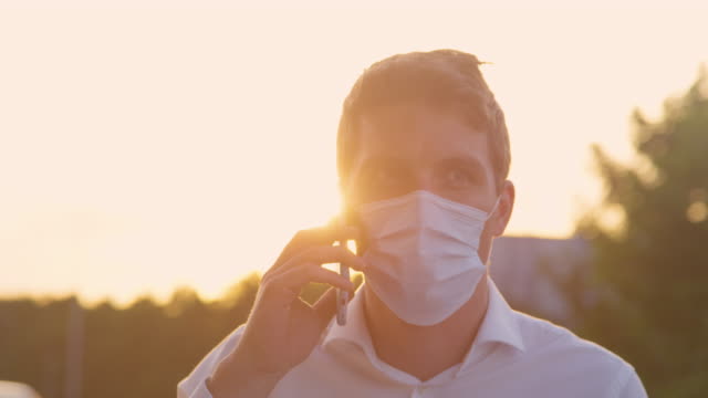 CLOSE-UP:-Young-man-talks-on-the-phone-while-wearing-a-disposable-surgical-mask.