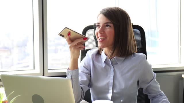 Confident-businesswoman-holding-smartphone-near-mouth-for-recording-voice-message-or-activating-digital-assistant.