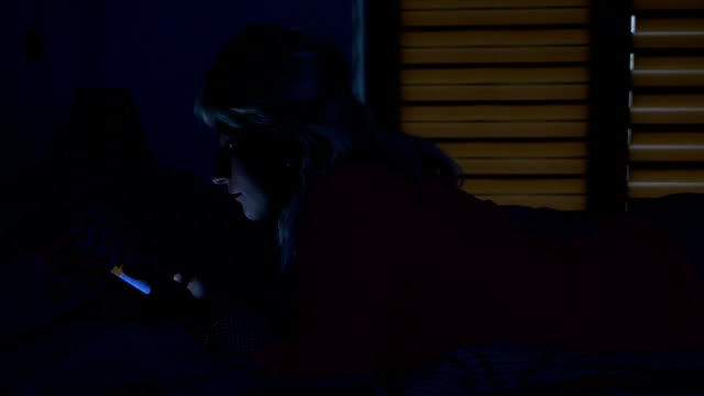 Frau-stehend-auf-dem-Bett-in-ihrem-Schlafzimmer-in-der-Nachtzeit-und-Scrollen-auf-ihrem-Smartphone