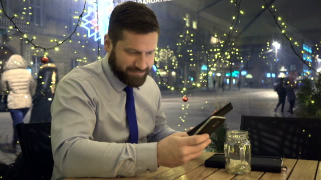 Businessman-browsing-tablet-answers-phone,-cafe,-evening,-christmas