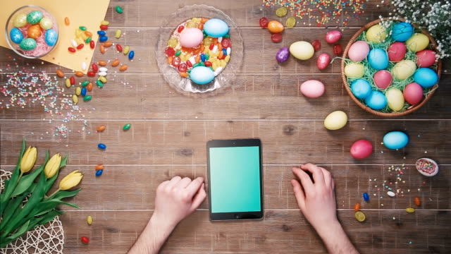 Mann-mit-digitalem-Tablet-auf-Tisch-mit-Ostereiern-dekoriert.-Top-View