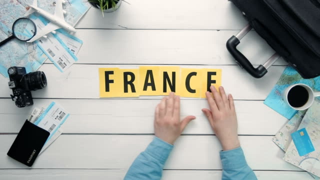 Top-view-time-lapse-hands-laying-on-white-desk-word-"FRANCE"-decorated-with-travel-items