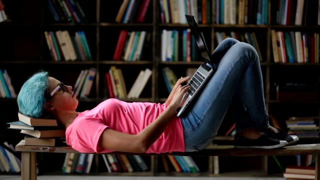 Nettes-Mädchen-mit-Laptop-auf-Bank-in-Bibliothek-liegend