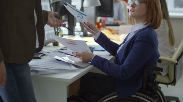 Mujer-en-silla-de-ruedas-sobre-documentos-de-negocios-con-un-colega-masculino