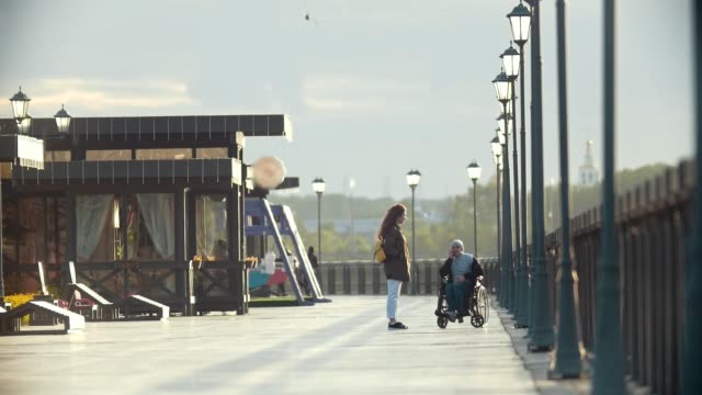 Hombre-discapacitado-en-silla-de-ruedas-hablar-por-teléfono,-caminar-juntos-a-su-novia-en-el-muelle
