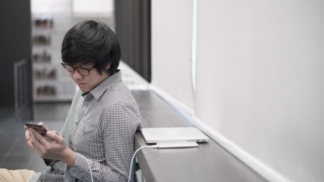 Junge-asiatische-Geschäftsmann-mit-Smartphone-auf-social-Media-Anwendung-während-des-Ladevorgangs-Gerät.-Urbaner-Lifestyle-in-Working-Space-Konzept.