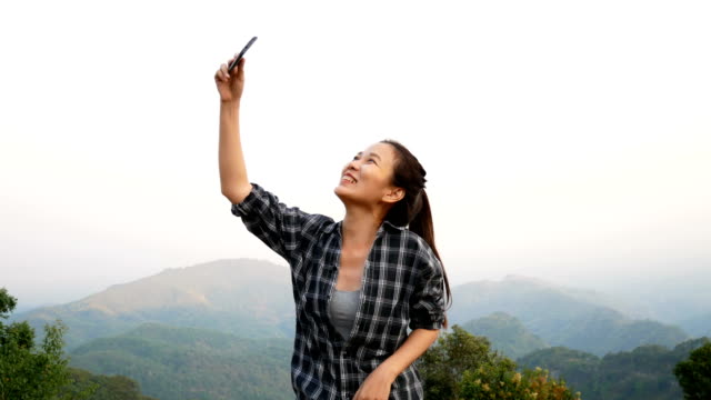 Imágenes-de-4K.-hermosa-mujer-asiática-que-video-chat-usando-el-teléfono-inteligente-al-aire-libre-compartiendo-viajes-naturaleza-vista-con-los-amigos-o-la-transmisión-en-vivo-a-través-de-los-medios-de-comunicación-social.