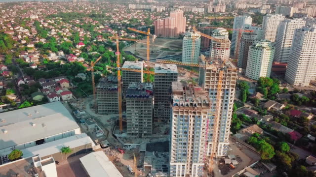 Aerial-drone.-Construction-of-high-rise-buildings-in-the-developing-area-of-a-large-city.-Sunset-shot.-In-the-picture,-construction-cranes-and-many-houses-under-construction.-wide-shot