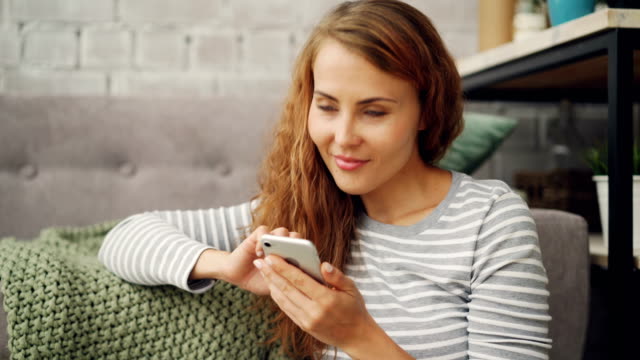 Glückliche-junge-Frau-hält-Smartphone-Bildschirm-berühren-und-lächelnd-social-Media-Konto-oder-Lesen-von-Nachrichten.-Moderne-Technologie-und-Millennials-Konzept.