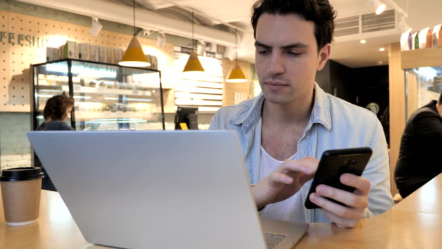 Joven-trabajando-en-la-computadora-portátil-y-usando-Smartphone-en-Café