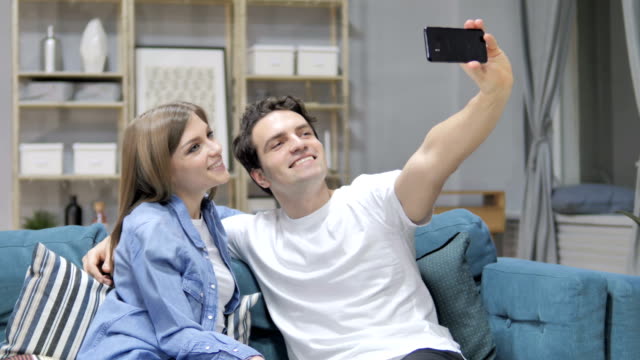 Joven-pareja-teniendo-Selfie-con-Smartphone-mientras-está-sentado-en-el-sofá