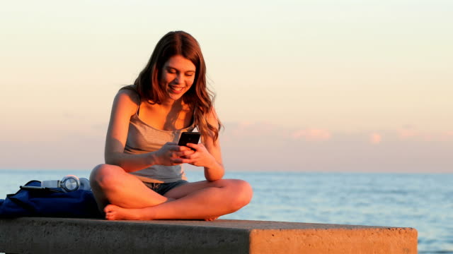 Teenager-Studentin-SMS-bei-Sonnenuntergang-am-Strand