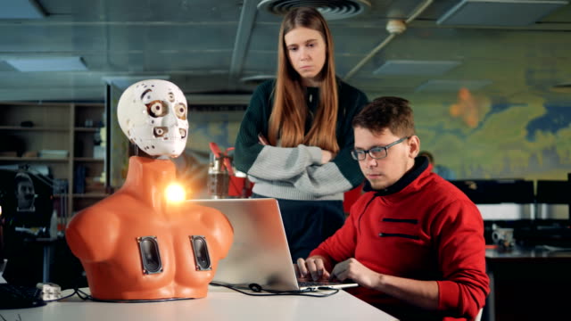 Man-and-woman-work-with-bionic-robot-in-a-room,-close-up.