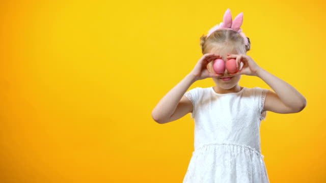 Happy-Easter-greetings,-smiling-little-girl-holding-colored-eggs-in-front-eyes