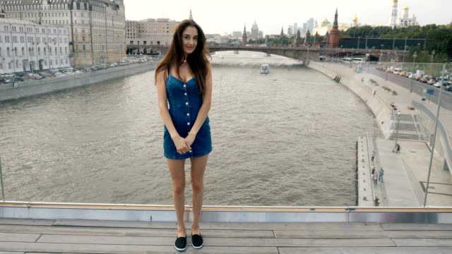 Brunette-woman-model-stand-bridge-river-looking-at-camera-and-sweet-smile-4k.