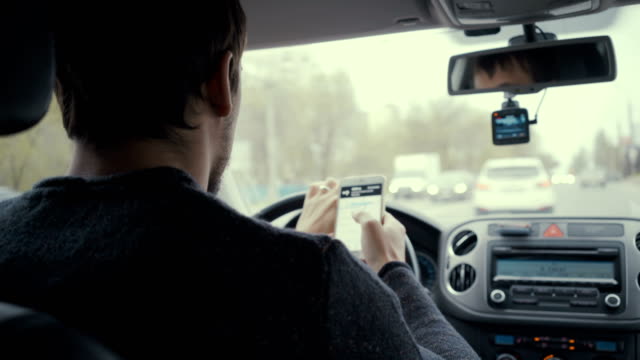 Junger-Mann-nutzt-Kartenapp-auf-seinem-Smartphone-in-einem-Auto-Fußjunge-Fahrerin-hinter-dem-Steuer.-4k