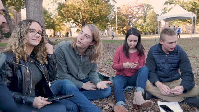 Studentinnen-und-Studenten-beim-Blick-auf-ihr-Handy-in-einer-Gruppe-im-Freien