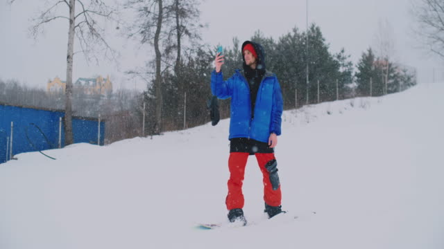 Disparo-a-cámara-lenta-de-un-snowboarder-usando-un-teléfono-inteligente-mientras-conduce-en-una-pista-de-esquí