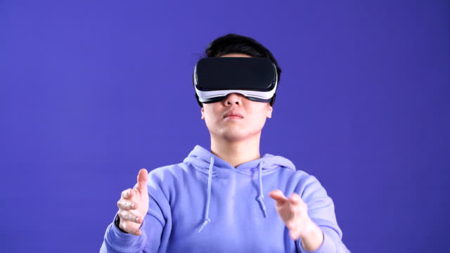 Fröhliche-japanische-Jugendliche,-die-Videospiel-in-virtueller-Reality-Helm-auf-dunkelblauem-Hintergrund-spielen