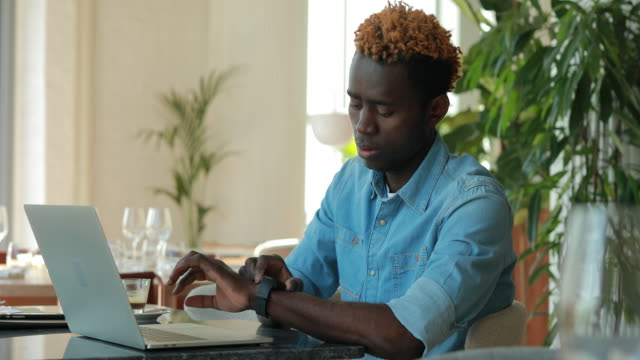 Afrikanischer-Amerikaner,-der-Laptop-im-Café-per-Handy-benutzt