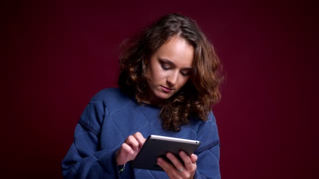 Closeup-portrait-of-young-caucasian-female-having-troubles-with-tablet-and-turning-on-the-good-music-on-the-touchpad-smiling
