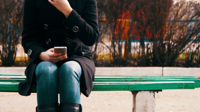 Junges-Mädchen-mit-einem-Handy-auf-einer-Bank-im-Stadtpark