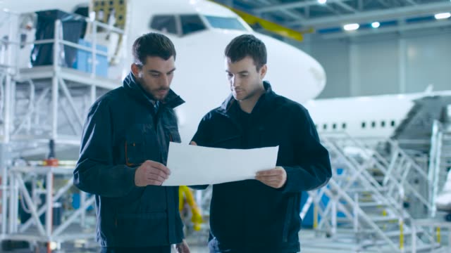 Team-von-Flugzeugmechanikern-und-Ingenieuren,-die-durch-die-Wartung,-das-Design-und-die-Entwicklung-von-Flugzeugen-wachen.-Profis-beraten-Blueprints-und-Talking