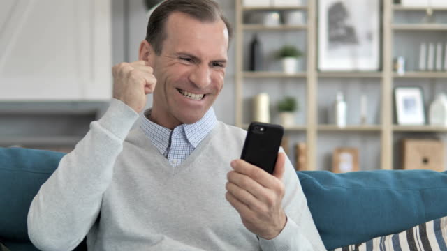 Hombre-de-mediana-edad-animar-en-el-teléfono-inteligente-mientras-está-sentado-en-el-sofá