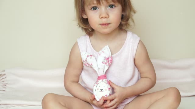 Portrait-of-cute-smiling-baby-girl-sits-and-shows-chicken-eggs-in-hands,-decorated-for-Easter-bunny,-with-painted-muzzle.