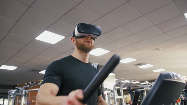 Joven-fuerte-haciendo-ejercicio-en-la-cinta-en-el-gimnasio,-usando-gafas-VR,-cámara-lenta