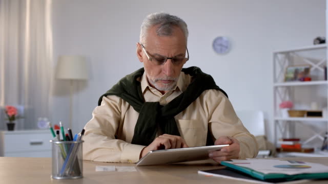 Old-man-entering-data-from-checks-into-tablet,-counting-budget-and-savings