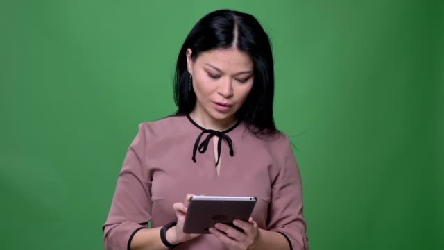 Closeup-shoot-of-young-attractive-asian-female-with-black-hair-using-the-tablet-with-background-isolated-on-green