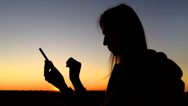 Frau-Silhouette-mit-Smartphone-in-der-Stadt-bei-Sonnenuntergang