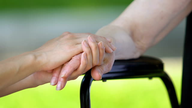 Daughter-supporting-her-disabled-mother-tenderly-stroking-her-hand,-close-up