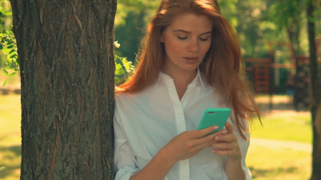 junge-Frau-posiert-in-der-Nähe-von-Baum-halten-mobil
