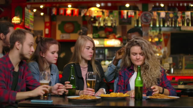 Eine-große-Gruppe-von-Freunden-in-der-Bar-sitzt-am-Tisch-lachend-und-plaudert-Bier-trinken