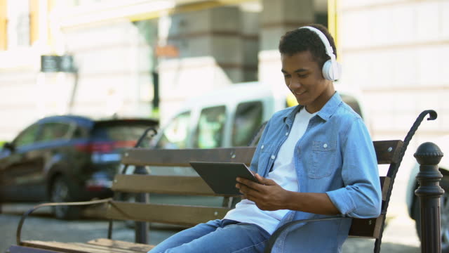 Mixed-race-guy-listening-to-music-in-headphones-and-scrolling-tablet,-resting