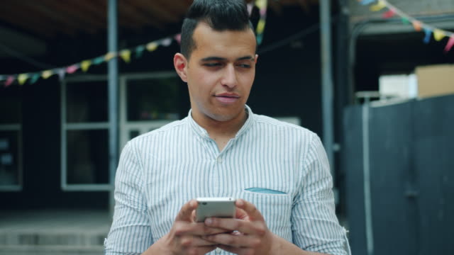 Portrait-of-handsome-mixed-race-man-using-smartphone-touching-screen-outside