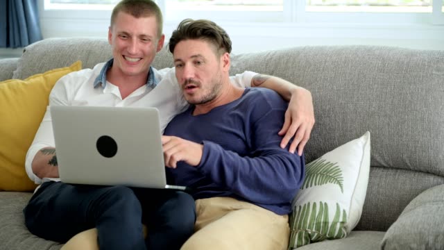 Pareja-gay-relajándose-en-el-sofá-usando-la-computadora-portátil.-Cabeza-sobre-hombro.