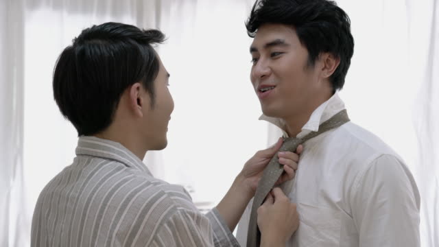 Asian-couple-gay-helping-tie-a-necktie-and-dress-to-work-in-morning-at-home.-Gay-boy-happy-emotion-and-hug-love-anniversary-together.-Concept-of-lifestyle,-family,-gay-and-bisexual.