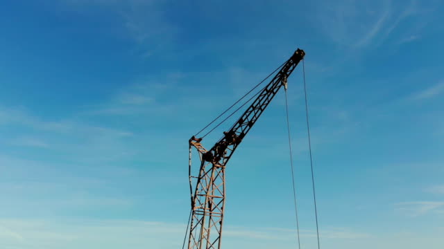 Two-construction-cranes-on-the-background-of-blue-sky-and-the-sun,-which-shines-in-the-camera-hiding-behind-the-construction-crane