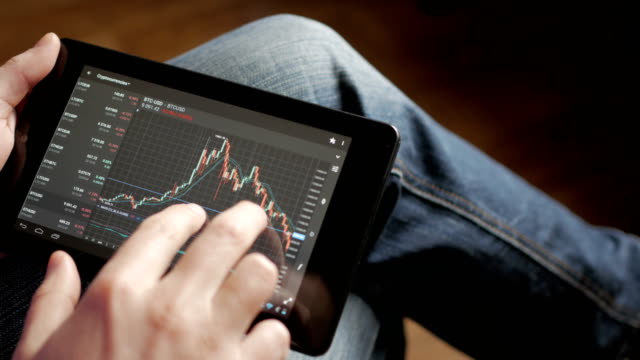 Stock-market,-trading-online,-trader-working-with-tablet-on-stockmarket-trading-floor.-Man-touching-screen,-browse-foreign-exchange-market-data,-chart.-Forex.-Crypto-currency.-Bitcoin-cryptocurrency.