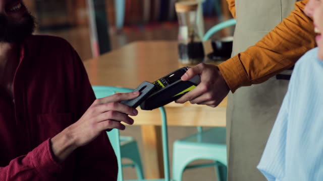 Close-up-man-paying-bill-with-contactless-smartphone-at-restaurant