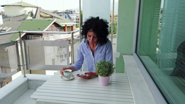 Geschäftsfrau-SMS-auf-dem-Smartphone-sitzend-am-Tisch-im-Café-trinken-einen-Kaffee