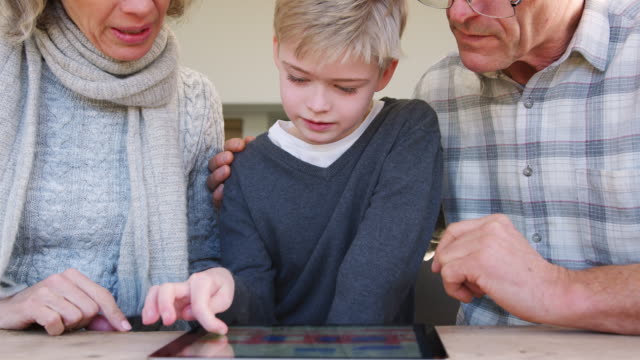 Nahaufnahme-von-Enkel-mit-Großeltern-spielen-auf-digitalen-Tablet-zu-Hause-zusammen