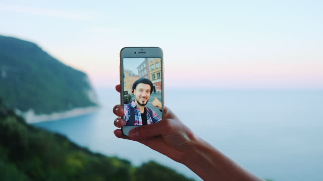 Hand-holding-smartphone-during-video-call-with-man-in-front-of-the-sea