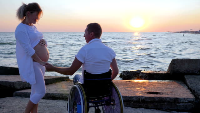 Glückliches-Paar-hält-Behinderten-im-Rollstuhl-Hand-schwangere-Mädchen