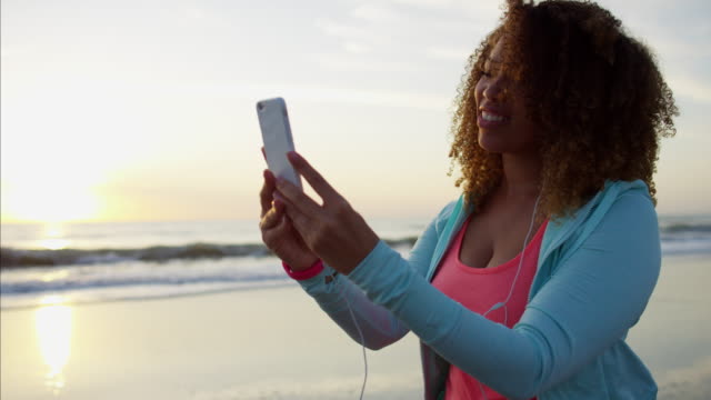 Ethnische-weiblich-zu-Fuß-am-Strand-mit-Smartphone